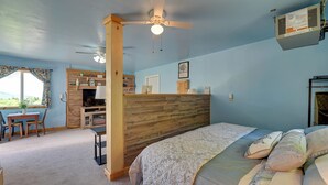 A bedroom with a bed, a desk, and a chair. There is a window with curtains, a ceiling fan, and a wall-mounted air conditioner. - Hike, Fish & Unwind! Catskills Studio w/ Mtn Views (Stamford)