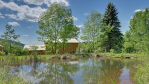 A rustic cabin with a pond in front, surrounded by trees and a clear sky. - Hike, Fish & Unwind! Catskills Studio w/ Mtn Views (Stamford)