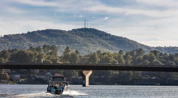 Une rivière avec un bateau passant sous un pont, entourée de collines et de maisons.