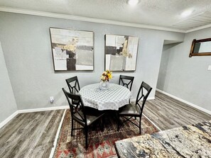 A dining area with a round table, four chairs, a vase with flowers, and two abstract paintings on the wall.