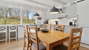 Een moderne keuken met witte kastjes, een houten eettafel en hangende hanglampen.