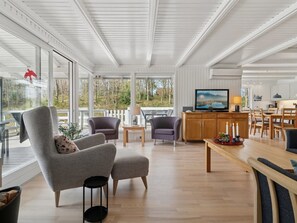 Een ruime woonkamer met een groot raam, een televisie en een eettafel met stoelen.