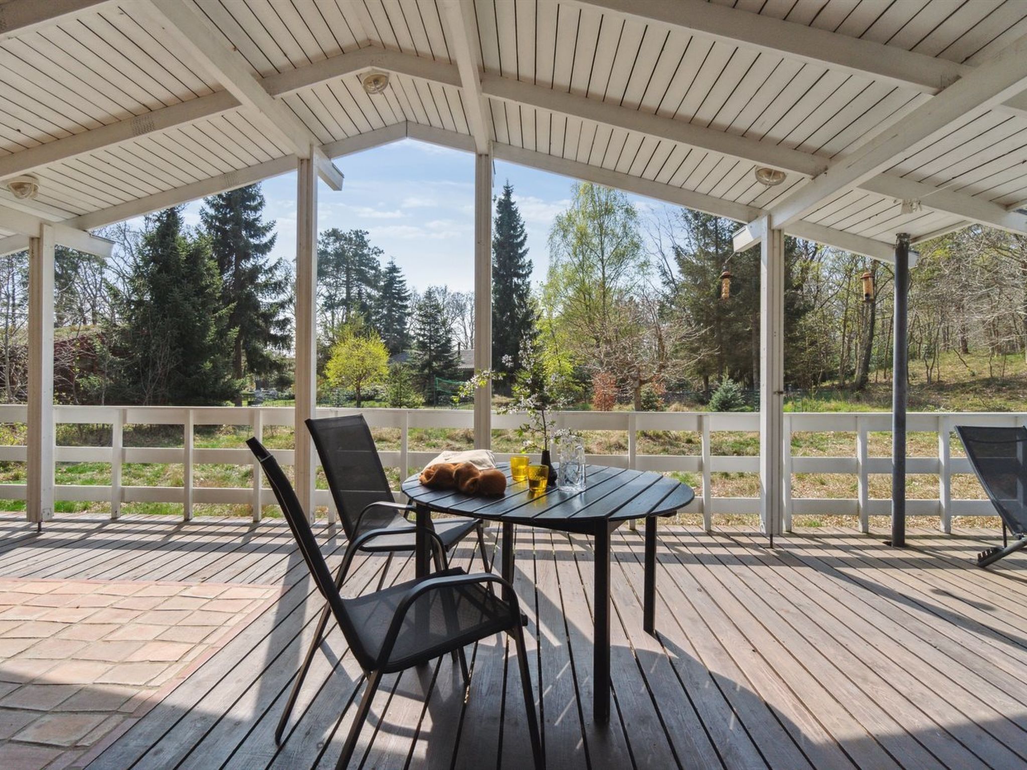 A covered outdoor deck with a table and chairs, overlooking a forested area.