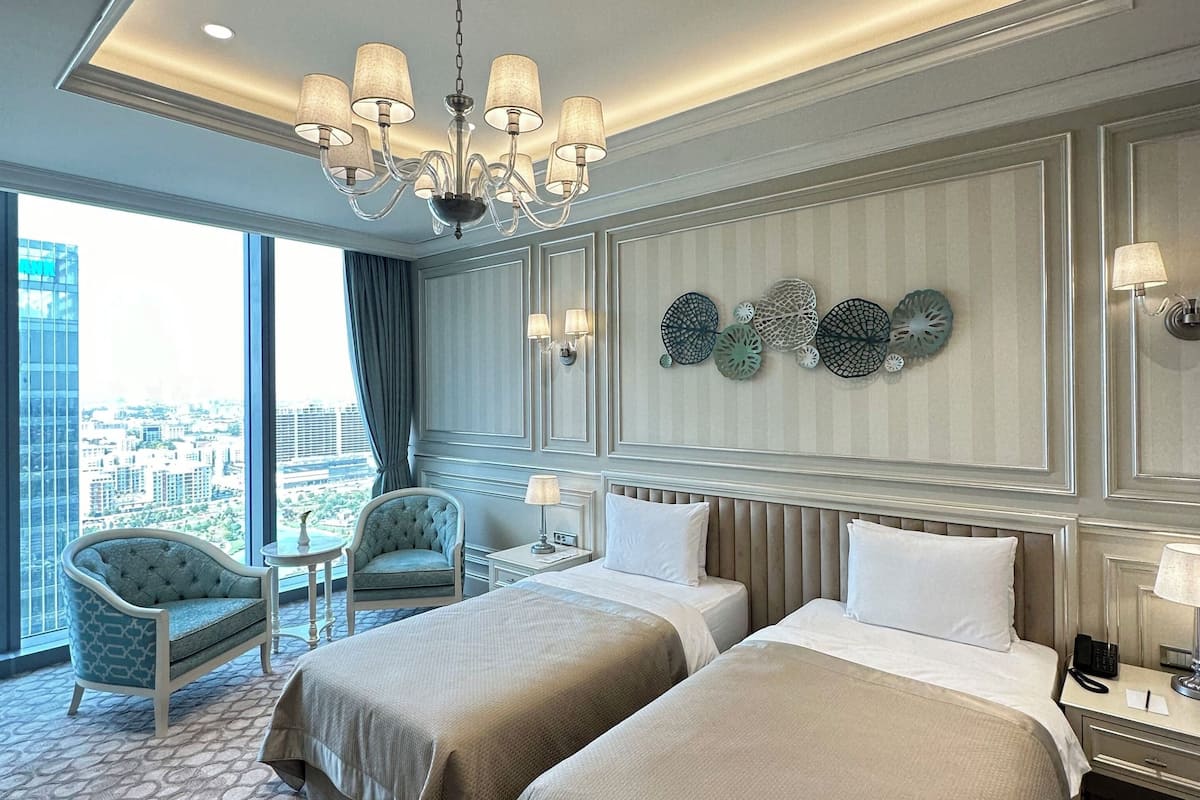 A hotel room with two beds, a chandelier, a view of the city, and a decorative wall.
