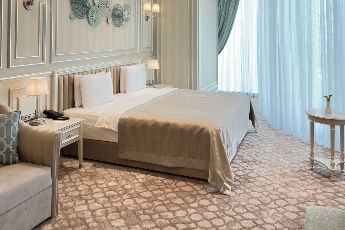 A hotel room with a large bed, a sitting area with a sofa, a small table, and a chandelier.