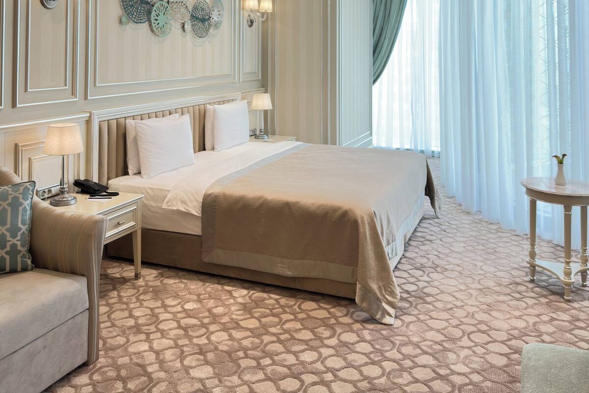 A hotel room with a large bed, a sitting area with a sofa, a small table, and a chandelier.