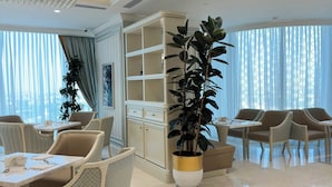 Een moderne hotellobby met een eetgedeelte, zitplaatsen, een grote potplant en een decoratieve plafondlamp.