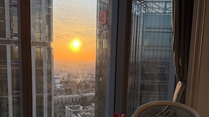 Een hotelkamer met een groot raam en uitzicht op de stad bij zonsondergang.