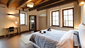 Une chambre avec un grand lit, deux fenêtres, un bureau et une chaise.