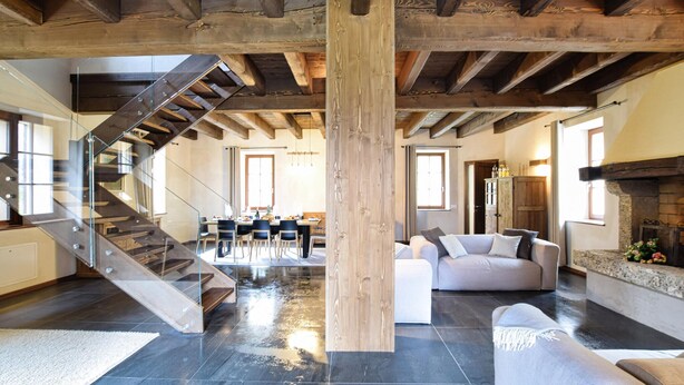 Un vaste espace de vie doté d’un haut plafond, de poutres apparentes en bois, d’un pilier central en bois, d’un escalier, d’un canapé et d’un coin repas.