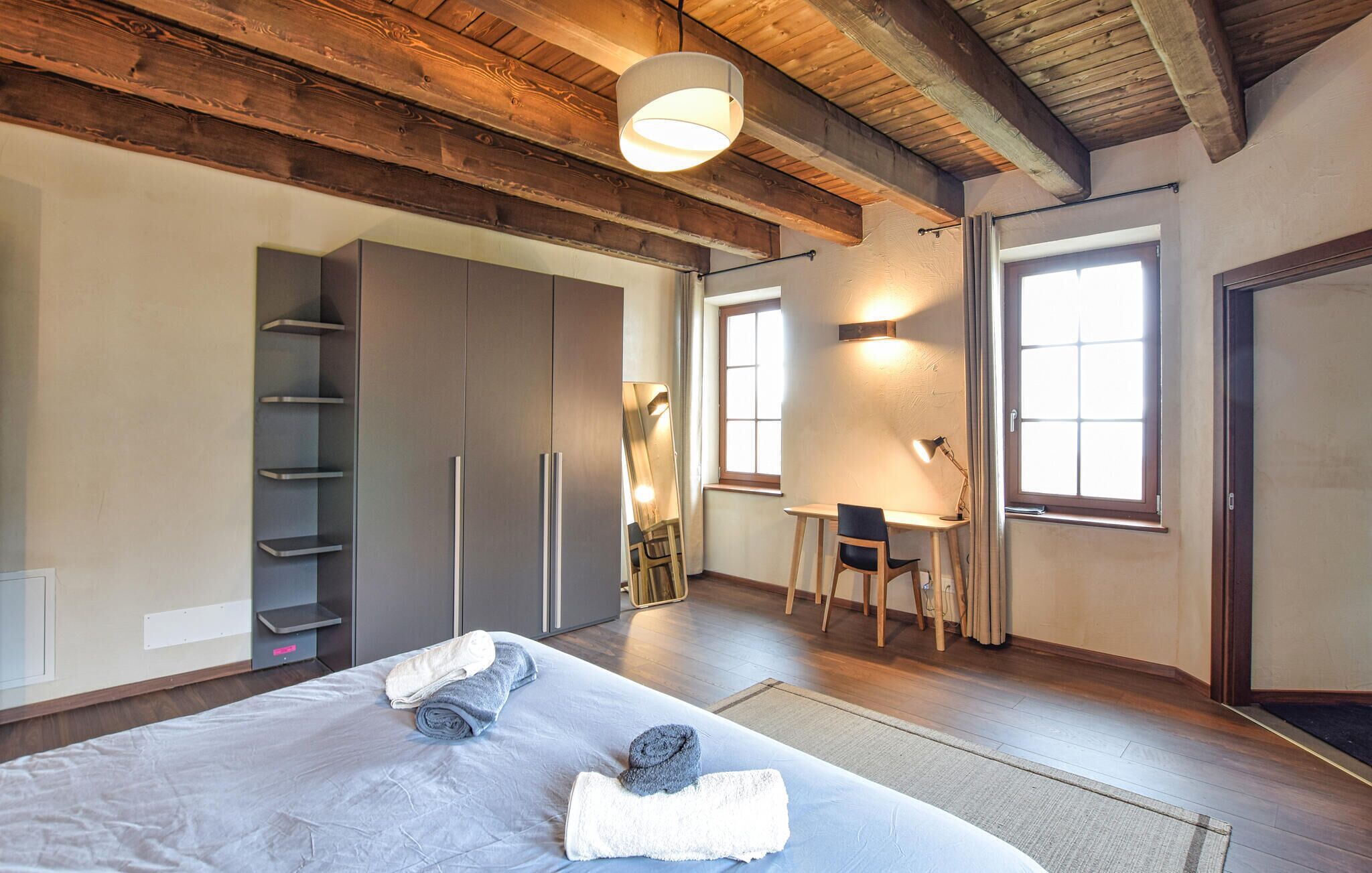 Une chambre à coucher avec un lit, un bureau et une chaise. On y trouve également une armoire et un miroir.