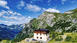 Un chalet de montagne à l’extérieur en bois, situé sur une colline et offrant une vue sur les montagnes environnantes et un ciel dégagé.