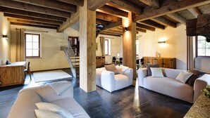 Un vaste espace de vie doté d’un haut plafond et de poutres apparentes, d’un escalier et d’un coin salon confortable.