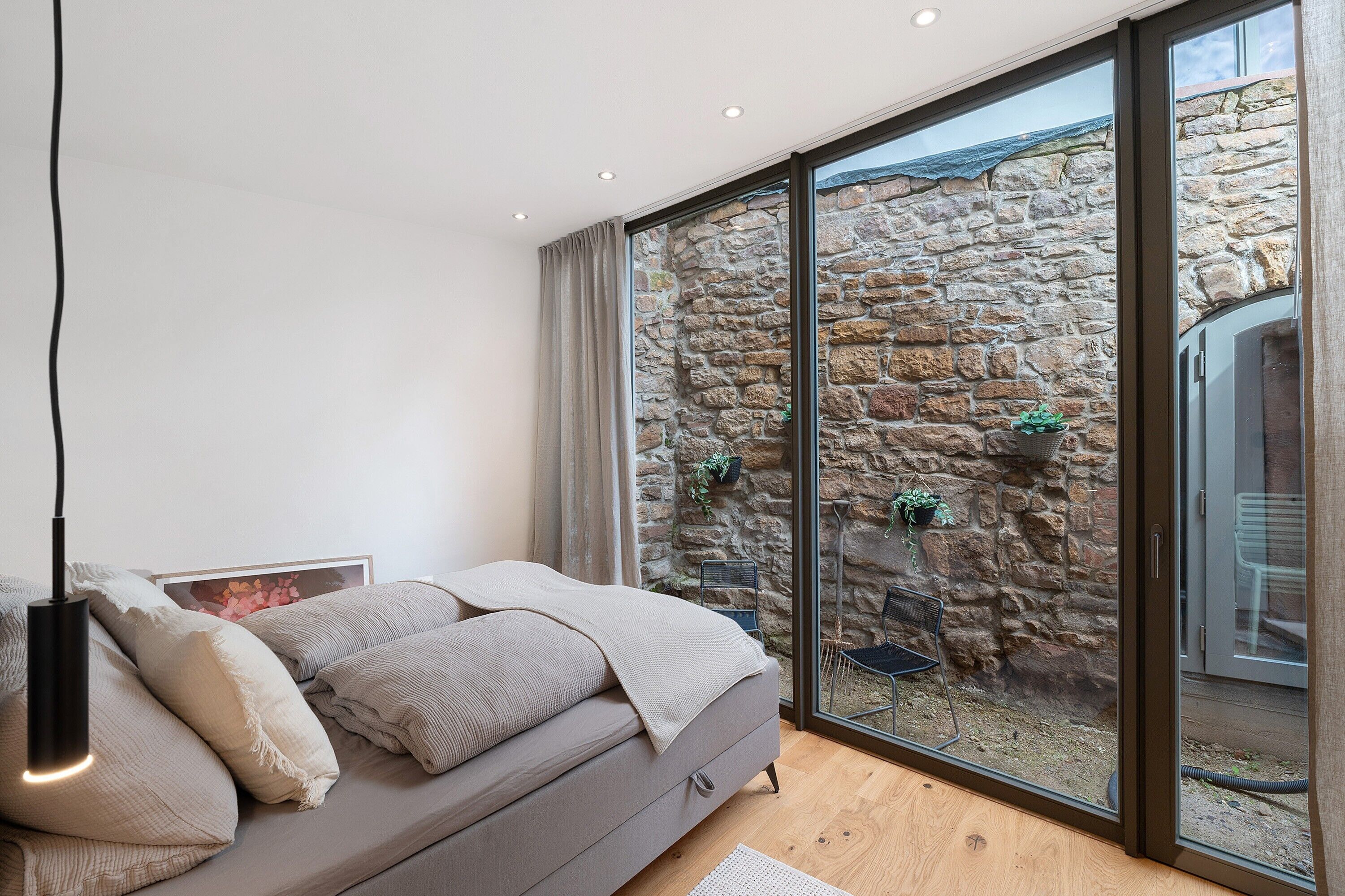 A bedroom with a bed, a bedside table, a lamp, a window, and a stone wall.