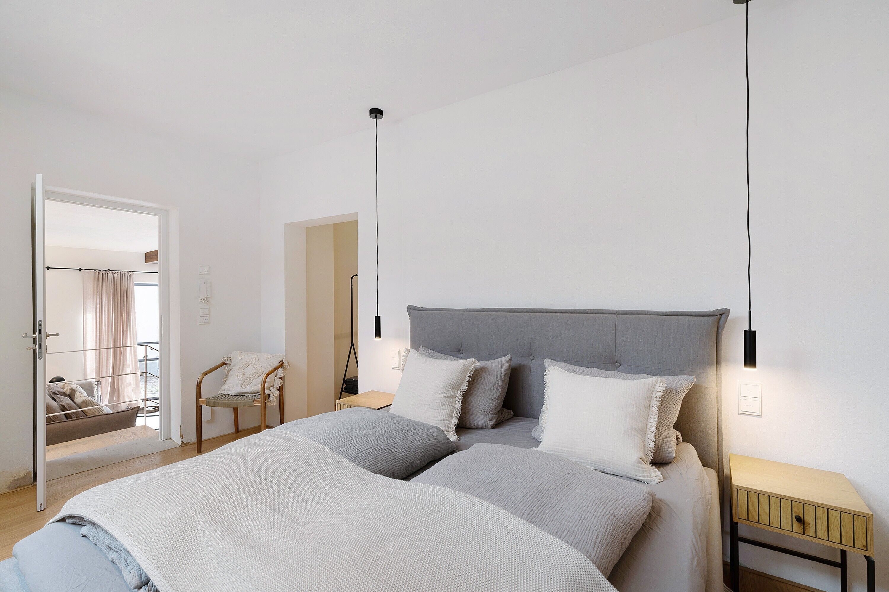 Une chambre à coucher comprenant un lit, des tables de chevet, une chaise et une porte donnant sur une autre pièce.