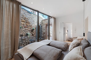 Un dormitorio con pared de piedra, ventanas amplias y una cama con muchos almohadones.