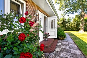 A brick house with a white door, a potted plant with red flowers, and a well-maintained lawn.