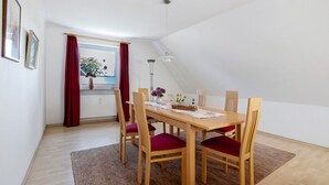 Uma área de refeições com mesa e cadeiras de madeira, uma janela com cortinas vermelhas e vista para o exterior.