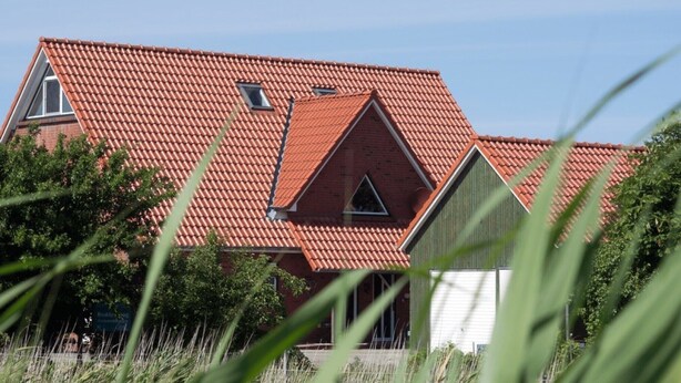Ein Haus mit rotem Ziegeldach, einem sichtbaren Schornstein und einem kleinen Fenster.