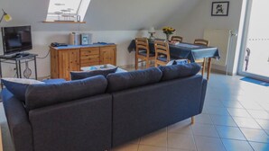Ein modernes Wohnzimmer mit einer Couch, einem Fernseher, einem Holzschrank, einem Esstisch mit Stühlen und einem Oberlicht.