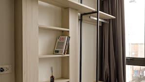A room with a built-in wooden shelving unit, a small bedside table, and a window with curtains. - HoLo Kim Ma Hanoi (Hanoi)