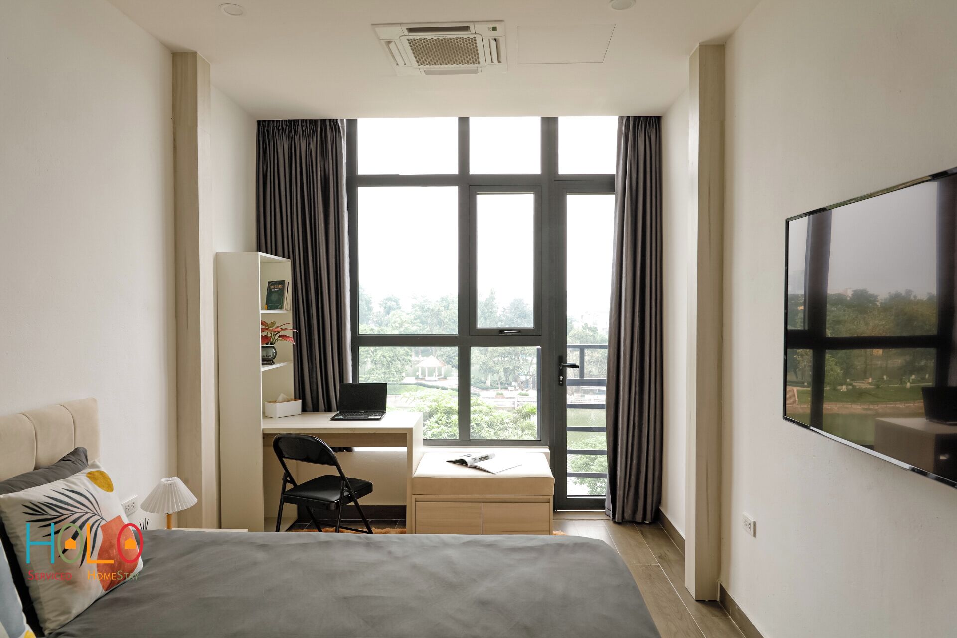 A hotel room with a bed, a desk, a chair, a TV, and a window with curtains.