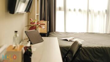 Hotelkamer met een bed, een bureau met een laptop, een fles, een tissuedoos en een plant in pot.