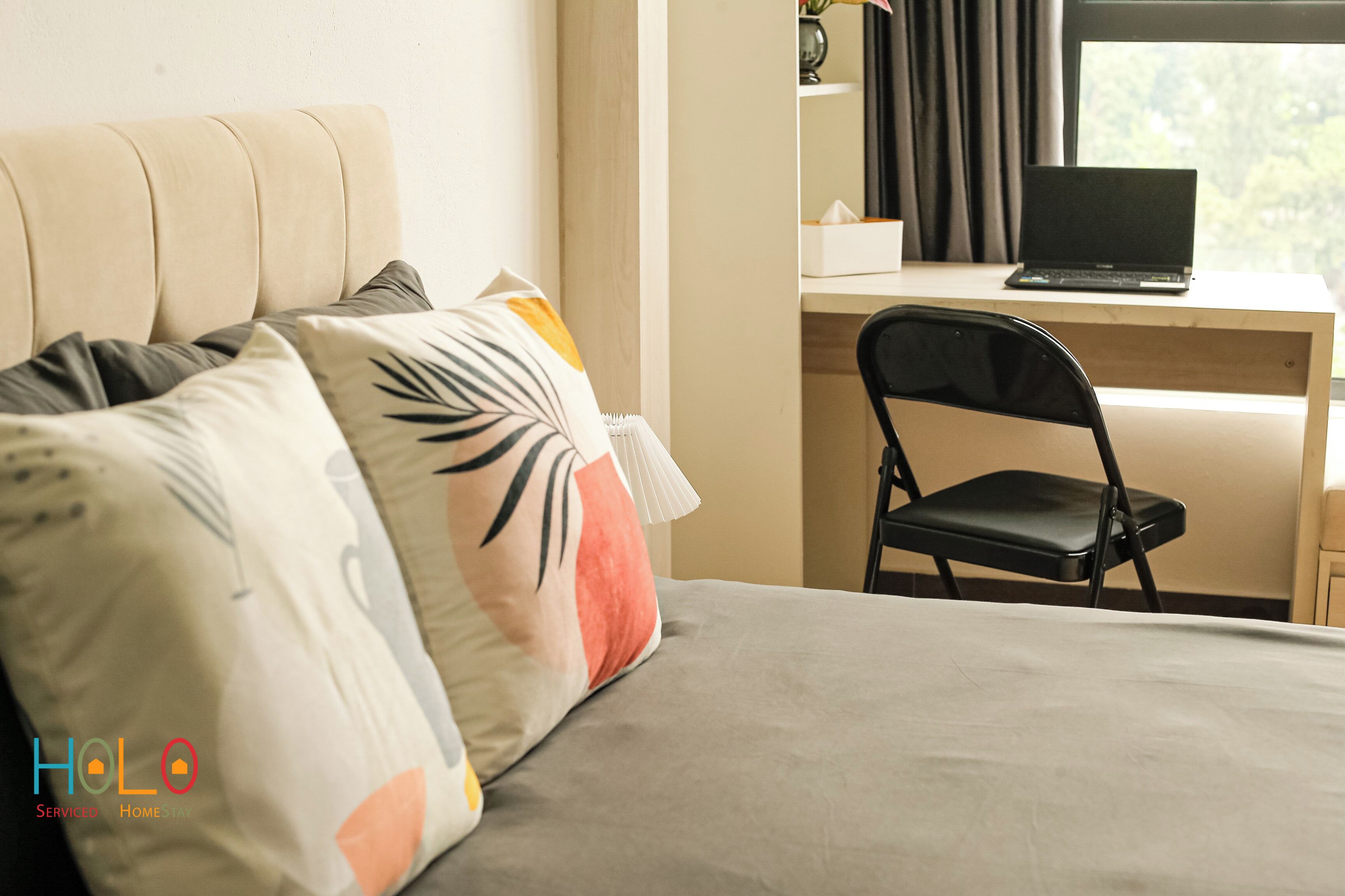 A bedroom with a bed, pillows, a desk with a laptop, and a chair.