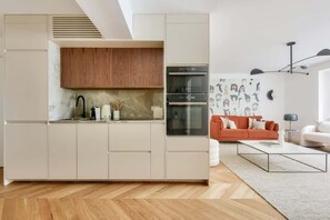 Cozinha moderna com eletrodomésticos embutidos, armário superior de madeira e área de refeições com sofá branco e mesa de centro.