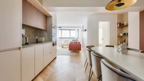 A modern kitchen with white cabinets, a dining area with a white table and chairs, and a large window providing natural light.