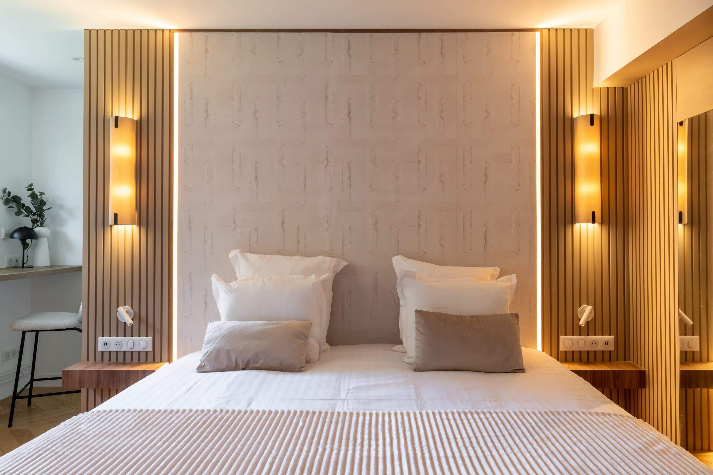A modern hotel room with a large bed, bedside tables, and wall-mounted lighting.