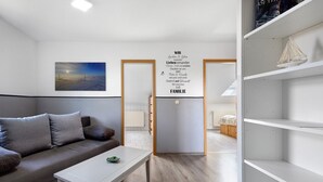 A modern living room with a grey sofa, a white coffee table, and a painting on the wall. There is a door leading to another room and a white shelf unit to the right. - Apartment 'Ferienwohnung Thomée' with Terrace and Wi-Fi (Looft)