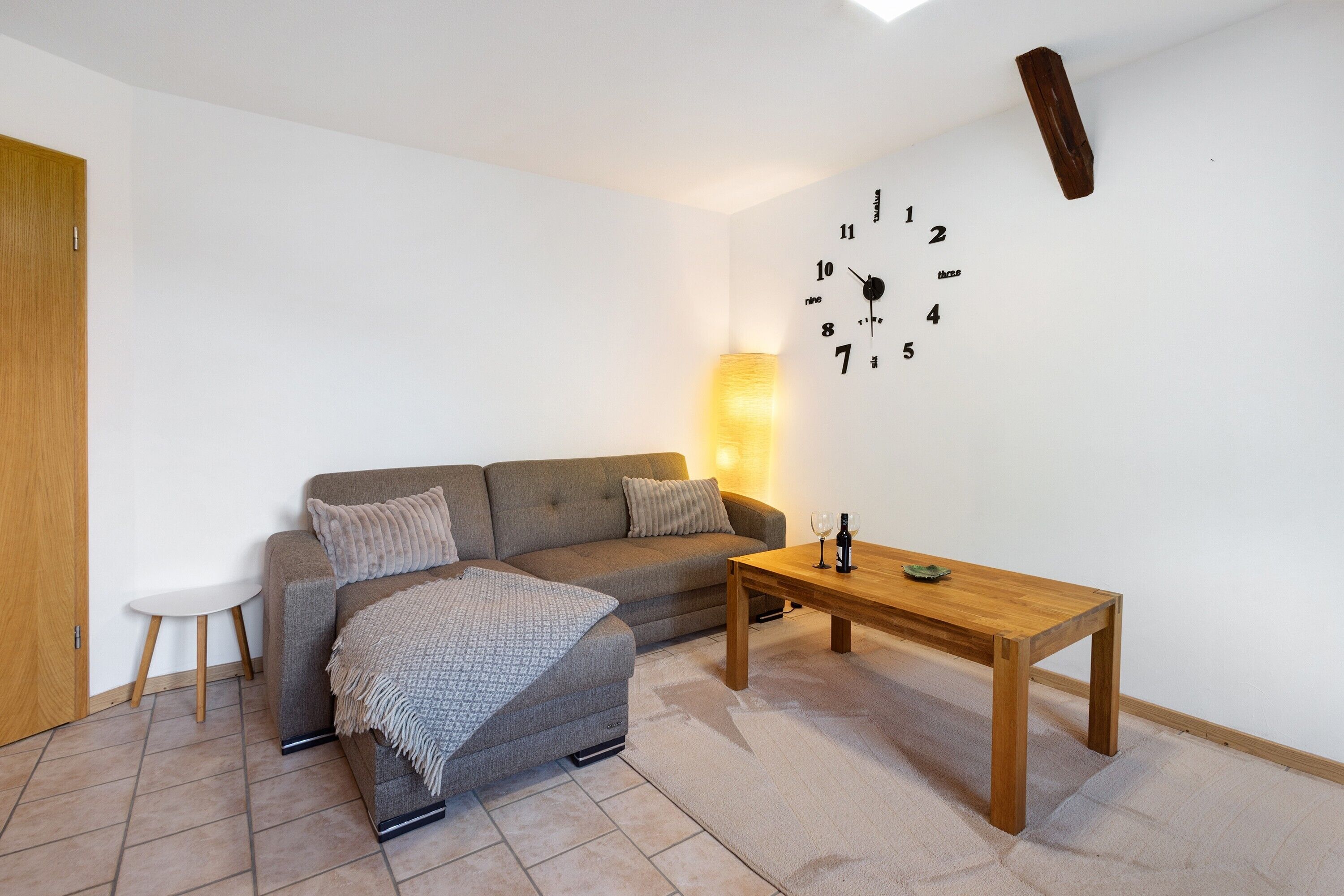 Un salon comprenant un canapé, un pouf, une table basse en bois et une horloge murale.