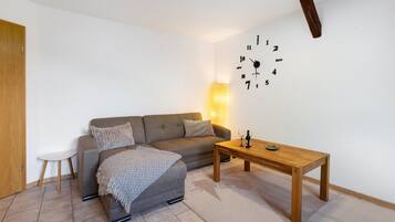A living room with a sofa, ottoman, wooden coffee table, and a wall clock.