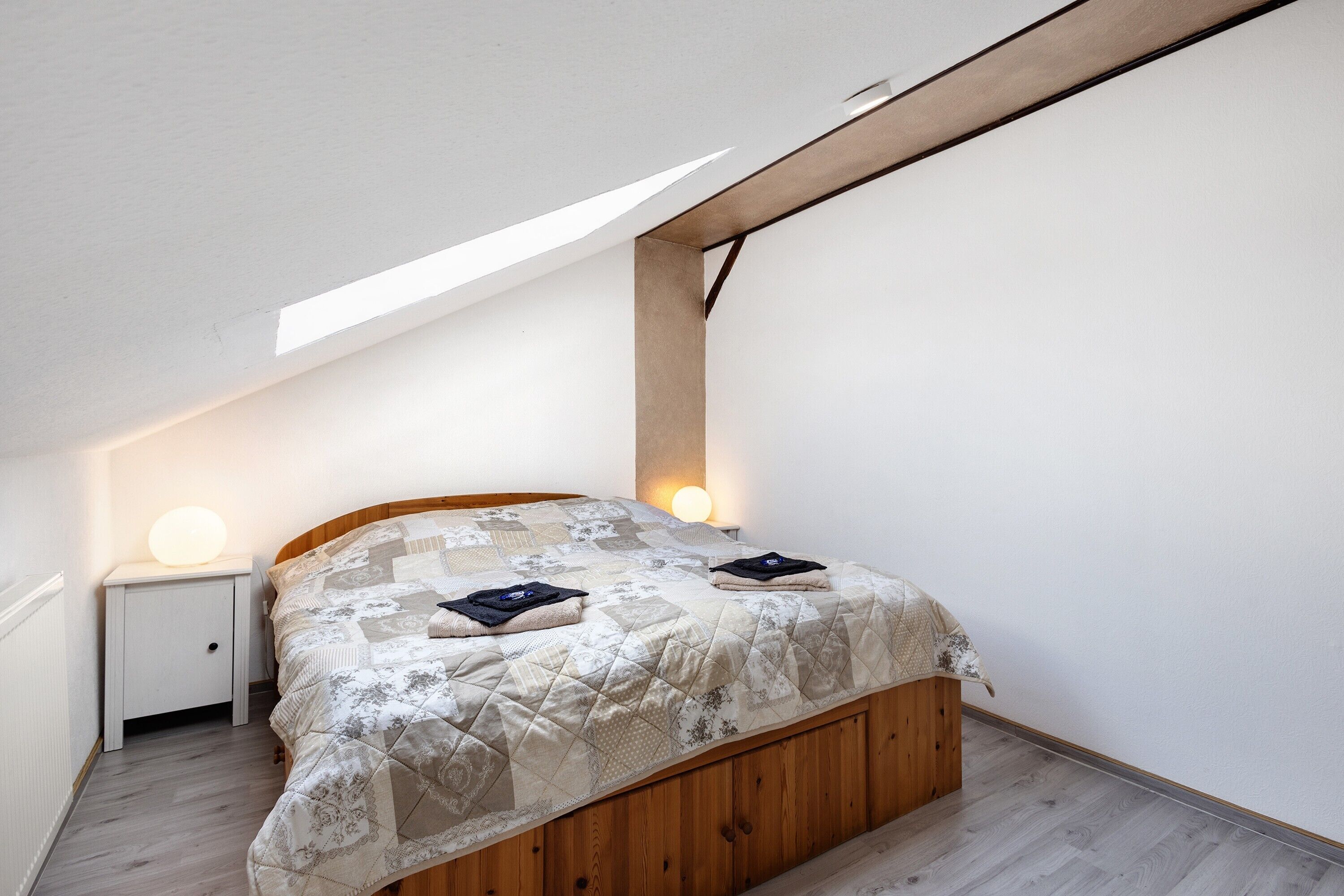 Ein Schlafzimmer mit einem Holzbett, einem weißen Nachttisch, einer Nachttischlampe und einem Oberlicht.