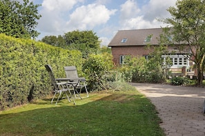 A brick house with a tiled roof, a paved pathway, and a lawn with a chair and table.