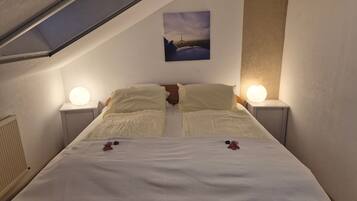 A bedroom with a sloped ceiling, two bedside lamps, a bed with a white bedspread, and a painting on the wall.