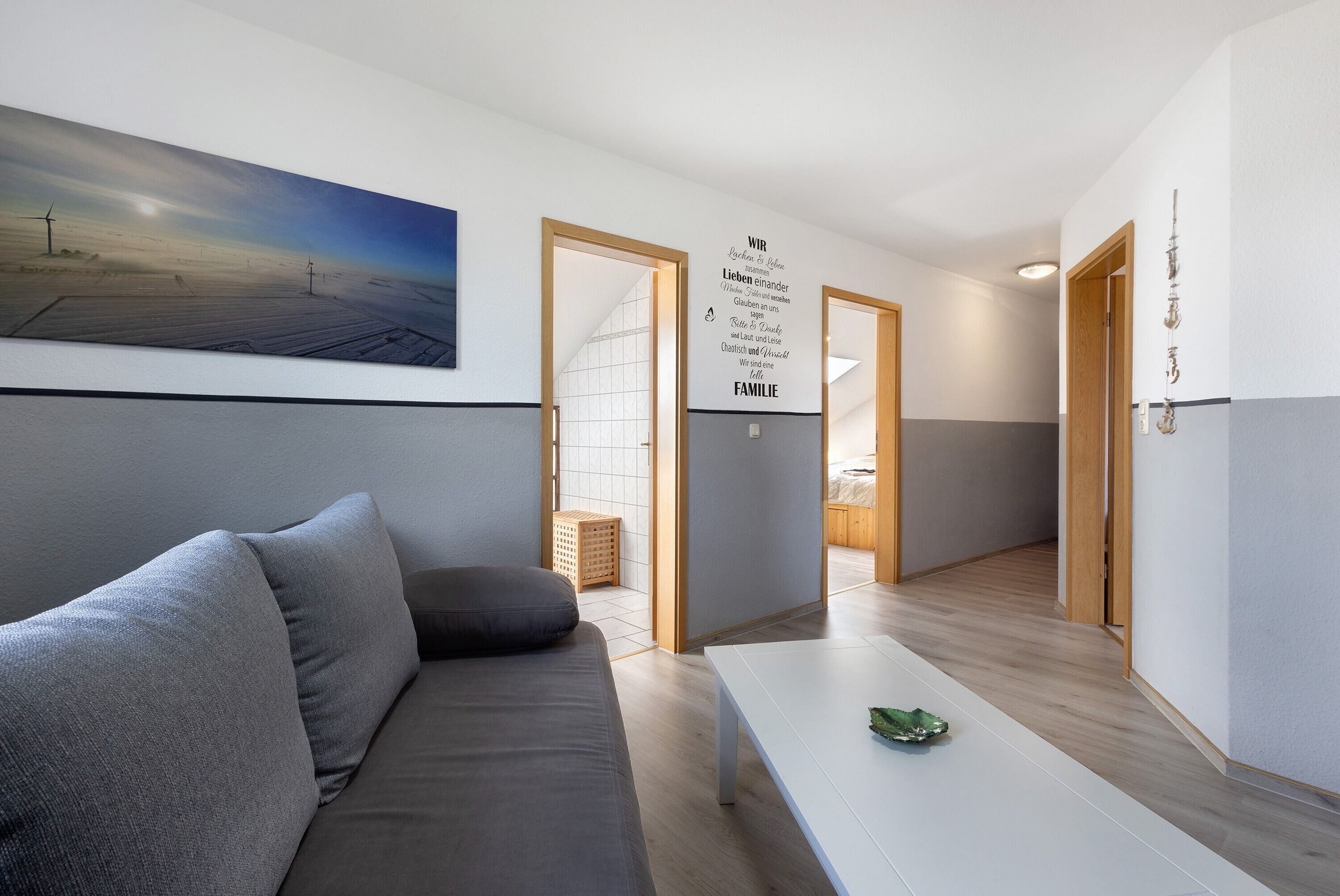 A modern living room with a gray sofa, a white coffee table, and a painting of a landscape.