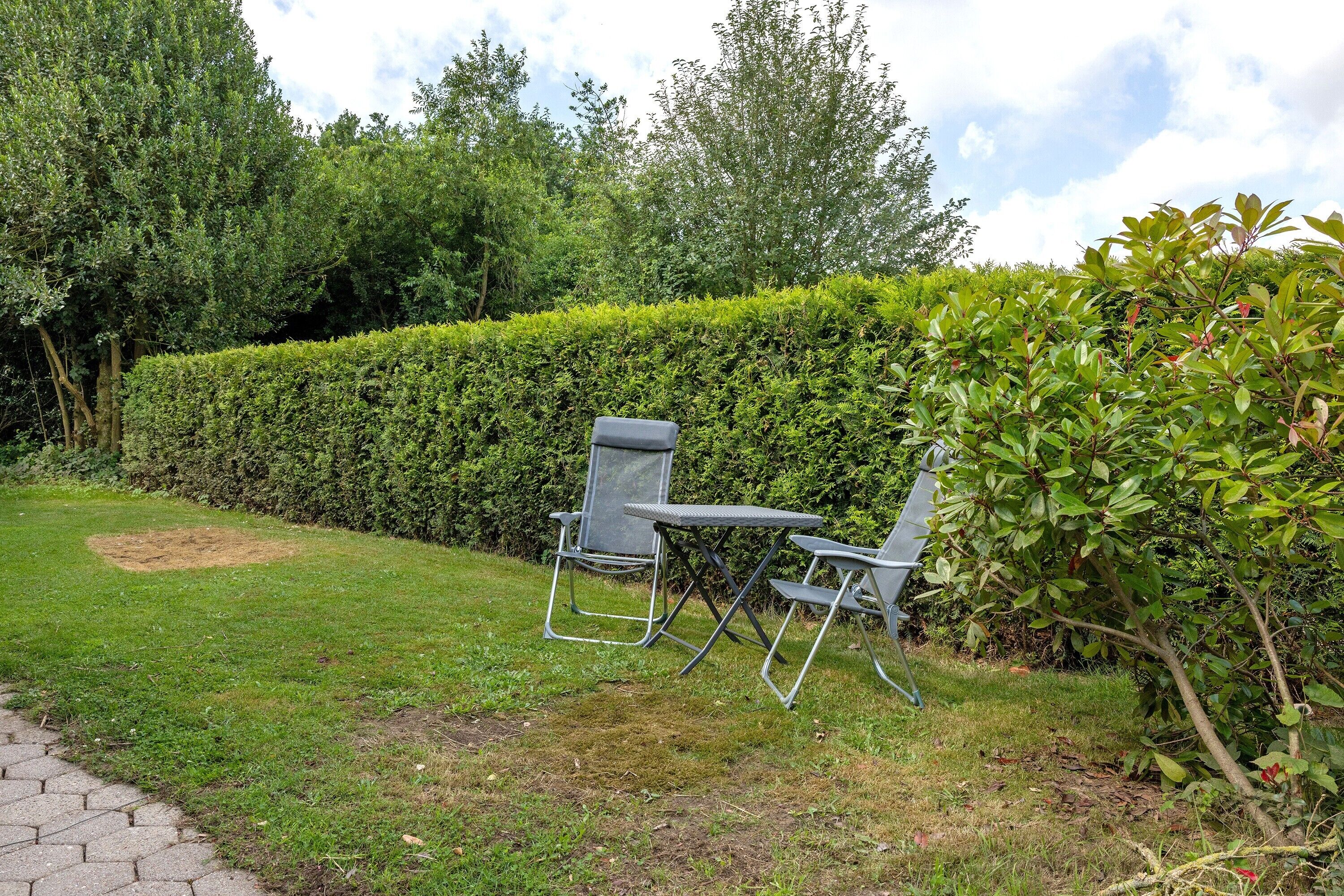 Ein Garten mit einer Hecke, zwei Klappstühlen und einem gepflasterten Weg.