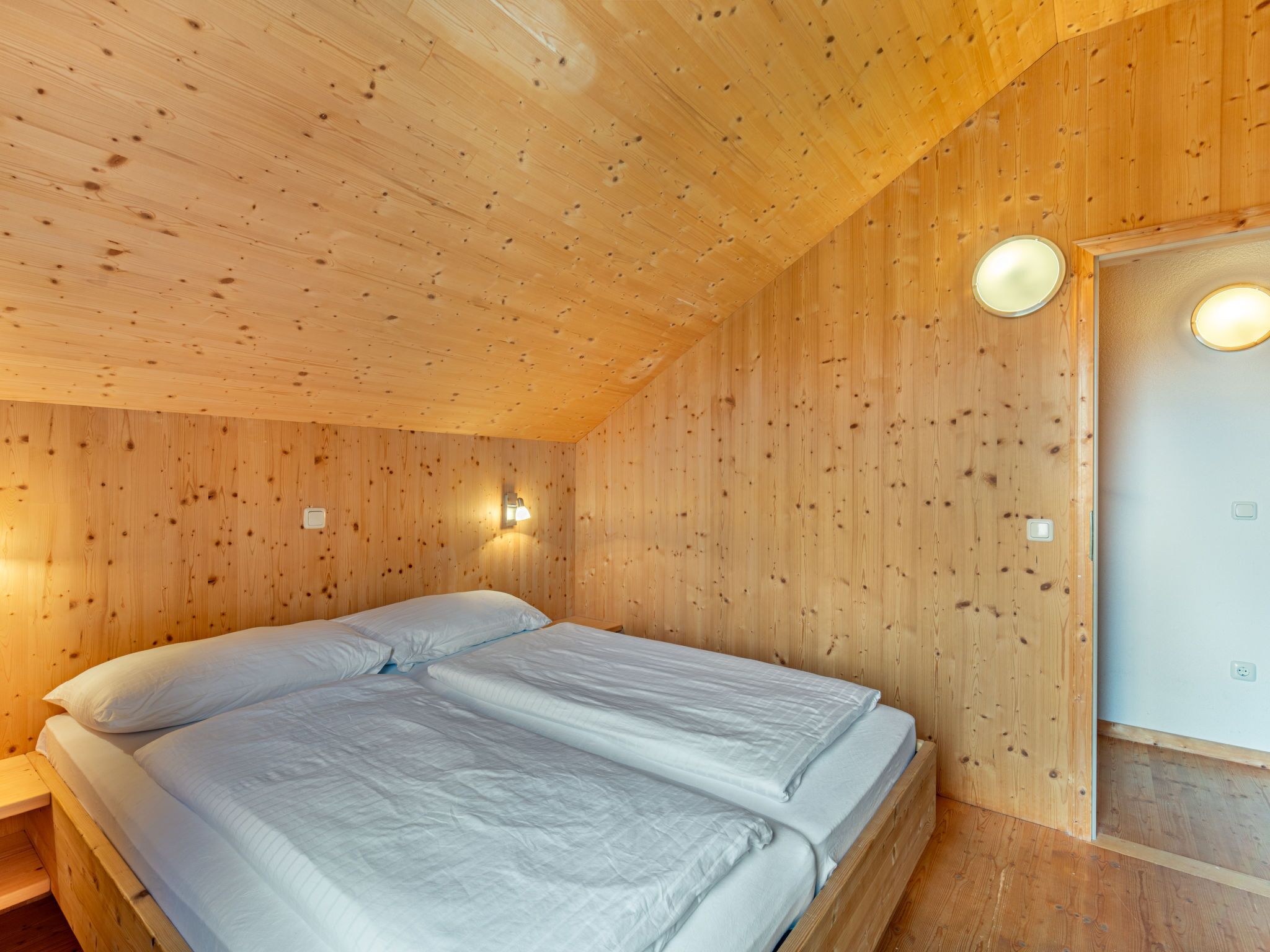 Une pièce de style cabane en bois, avec un lit, deux lampes fixées au mur et une porte.