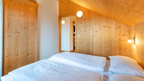 Un dormitorio con paredes y techo de madera, dos camas y una lámpara redonda.