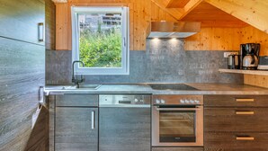 Una cocina moderna con armarios de madera, horno empotrado, pileta y ventana con vista a la vegetación.