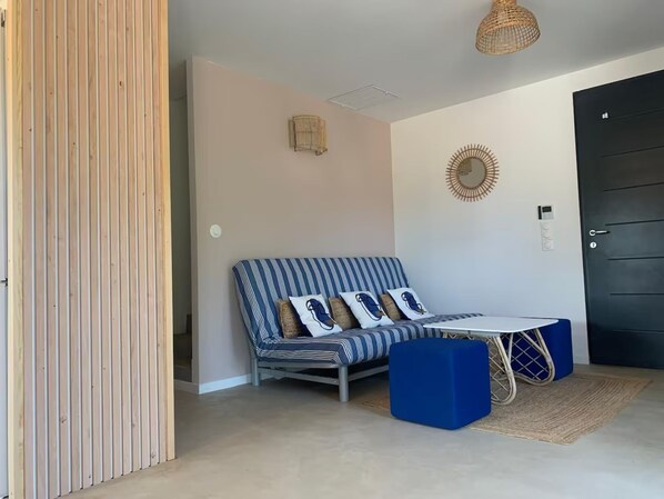 A room with a striped sofa, a small table, a wicker chair, a door, and a wall clock.