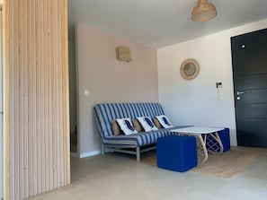 A room with a striped sofa, a small table, a wicker chair, a door, and a wall clock.