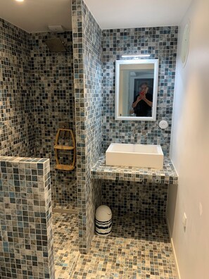 A bathroom with a tiled shower, a sink, and a mirror.