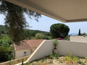 A residential area with a sloped roof, a large tree, and a view of a distant landscape.