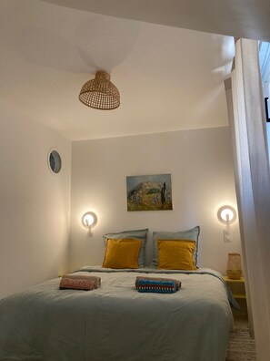 A bedroom with a bed, two bedside lamps, a painting on the wall, and a hanging light fixture.
