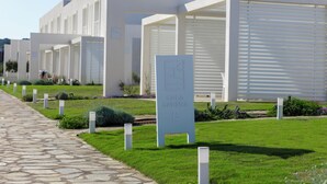 A row of modern, white buildings with a stone pathway leading to them. Each building has a sign indicating a room number.