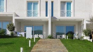 A modern hotel with a stone pathway leading to a double door entrance, white outdoor furniture, and a clear view of the surrounding landscape.