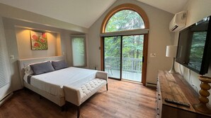 Un dormitorio con cama, ventilador de techo, televisión y balcón con vista a árboles.